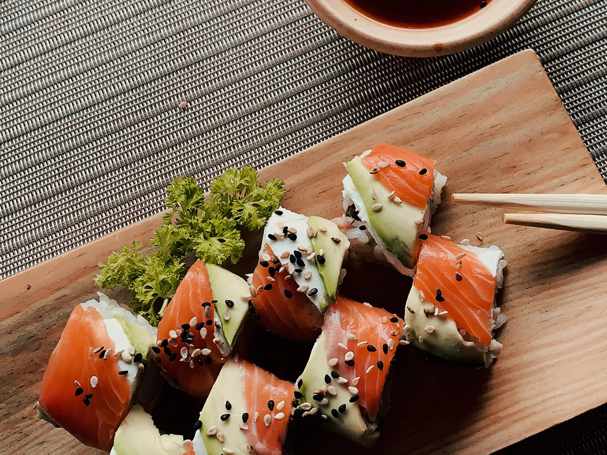 Salmon cream cheese sushi rolls topped with sesame seeds on wooden serving board with chopsticks at NIGIRI BAR JAPANESE RESTAURANT, a Japanese Restaurant in Jacksonville